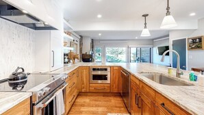 Una cocina moderna con armarios de madera, electrodomésticos de acero inoxidable, encimera de mármol e iluminación colgante.