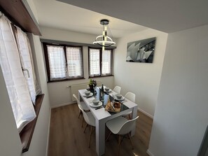 Ein Essbereich mit einem Tisch für vier Personen, einer modernen Pendelleuchte und einem Fenster mit Vorhängen.