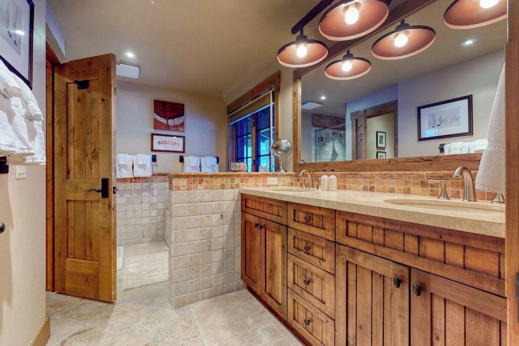 Un baño con armarios de madera, un espejo grande y salpicadero de azulejos.