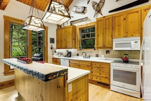 A kitchen with wooden cabinets, a white countertop, a stove, and a microwave. - Spacious Cozy Cabin w/ Deck, Private Hot Tub, Grill - Amazing In-Village Locale (Teton Village)