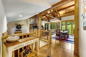 A spacious loft-style room with a high ceiling, wooden beams, a fireplace, and large windows offering a view of the outdoors. - Spacious Cozy Cabin w/ Deck, Private Hot Tub, Grill - Amazing In-Village Locale (Teton Village)