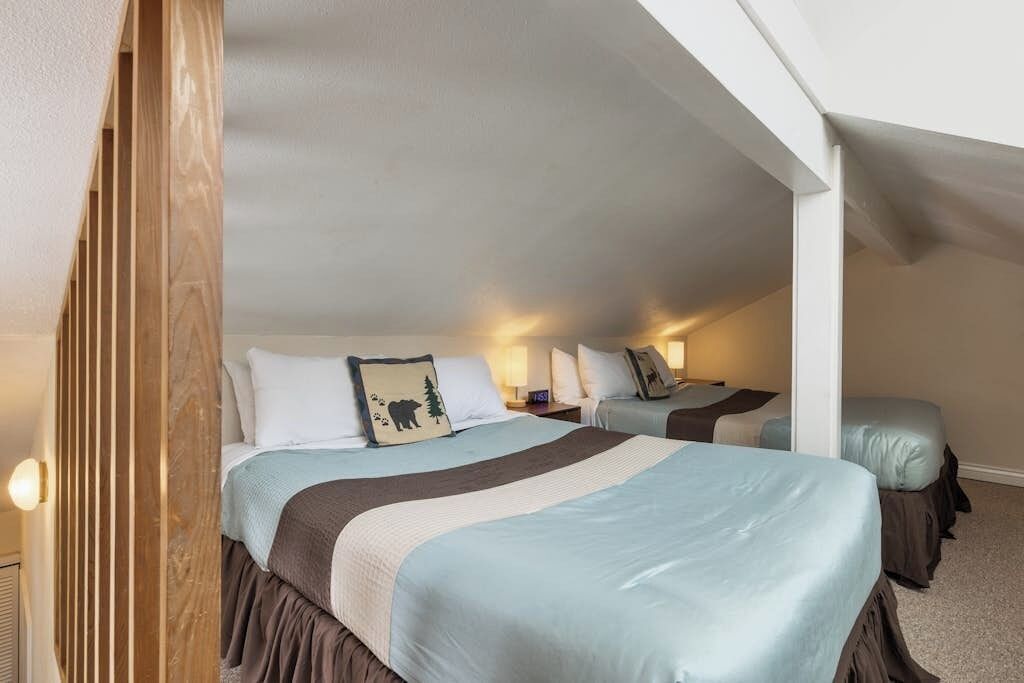Quarto de hotel com duas camas, um separador de madeira e uma mesa de cabeceira com luminárias.
