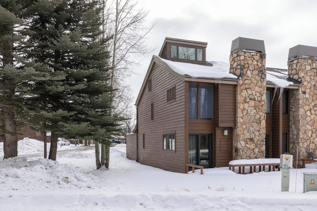 Ein modernes, zweistöckiges Gebäude mit einem Steinkamin, Holzverkleidung und einem mit Schnee bedeckten Dach.