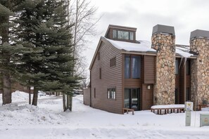 A modern two-story building with a stone chimney, wooden siding, and a snow-covered roof. - Inviting condo with mountain views, great location & fireplace (Jackson)