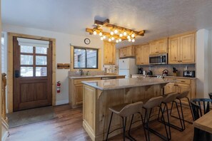 A kitchen with wooden cabinets, a central island with bar stools, a microwave, and a clock on the wall. - Inviting condo with mountain views, great location & fireplace (Jackson)