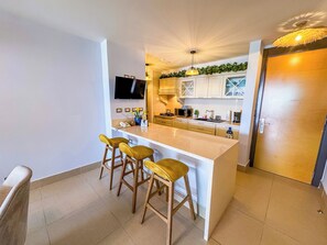 A modern kitchen with a central island, bar stools, a flat-screen TV, and a microwave. - Stunning Beachfront Condo in P.H. Bahia (Nueva Gorgona)