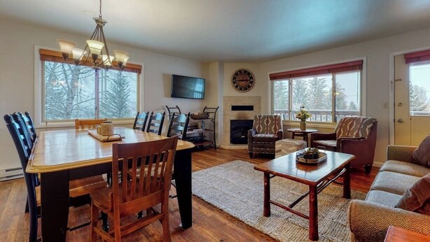 A spacious living room with a dining table, chairs, a fireplace, a television, and large windows.