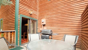 Une terrasse avec une table ronde et des chaises, un barbecue et un mur en bois recouvert de lambris horizontaux.