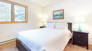 Une chambre à coucher avec un lit, deux tables de chevet avec des lampes, une fenêtre et un tableau au mur.