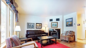 Un salon comprenant un canapé, un fauteuil, une table basse, une cheminée et des tableaux encadrés accrochés au mur.