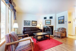 A living room with a sofa, armchair, coffee table, fireplace, and framed pictures on the wall. - Roomy 2-story home with furnished deck, grill, fireplace, & great location (Jackson)