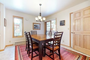 A dining room with a wooden table and chairs, a chandelier, and a large window. - Roomy 2-story home with furnished deck, grill, fireplace, & great location (Jackson)