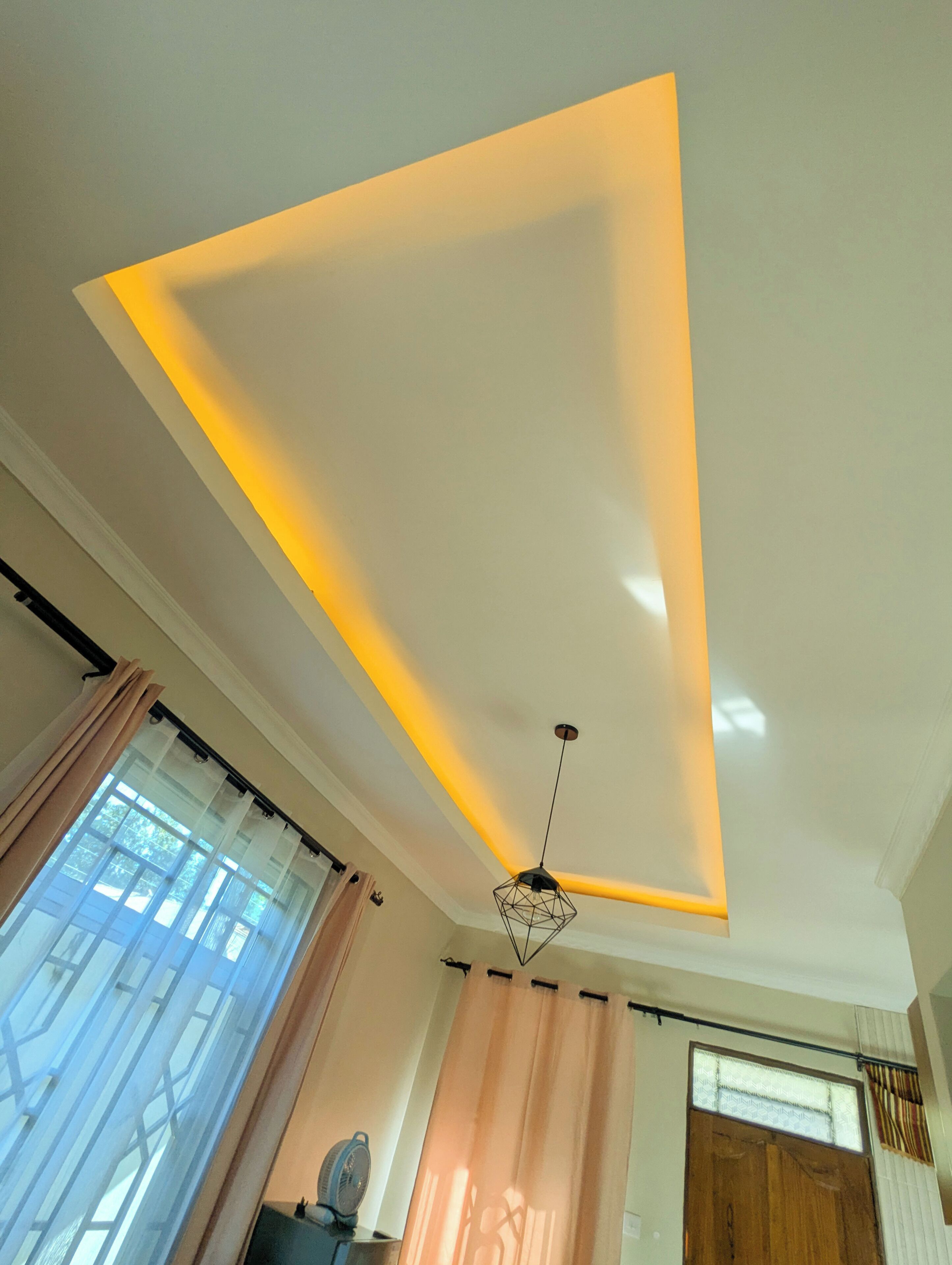 A room with a ceiling light fixture, a window with curtains, and a door with a window.