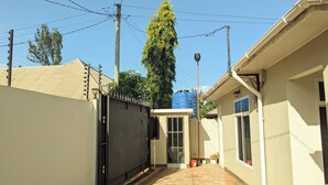 A narrow alleyway with a gated entrance, a tiled pathway, and a building with a window and a door. - Zebra Nest Apartpment (Kilimanjaro Region)