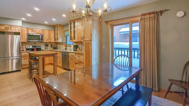 Una cocina con gabinetes de madera, un refrigerador de acero inoxidable, un microondas y una mesa de comedor con sillas.