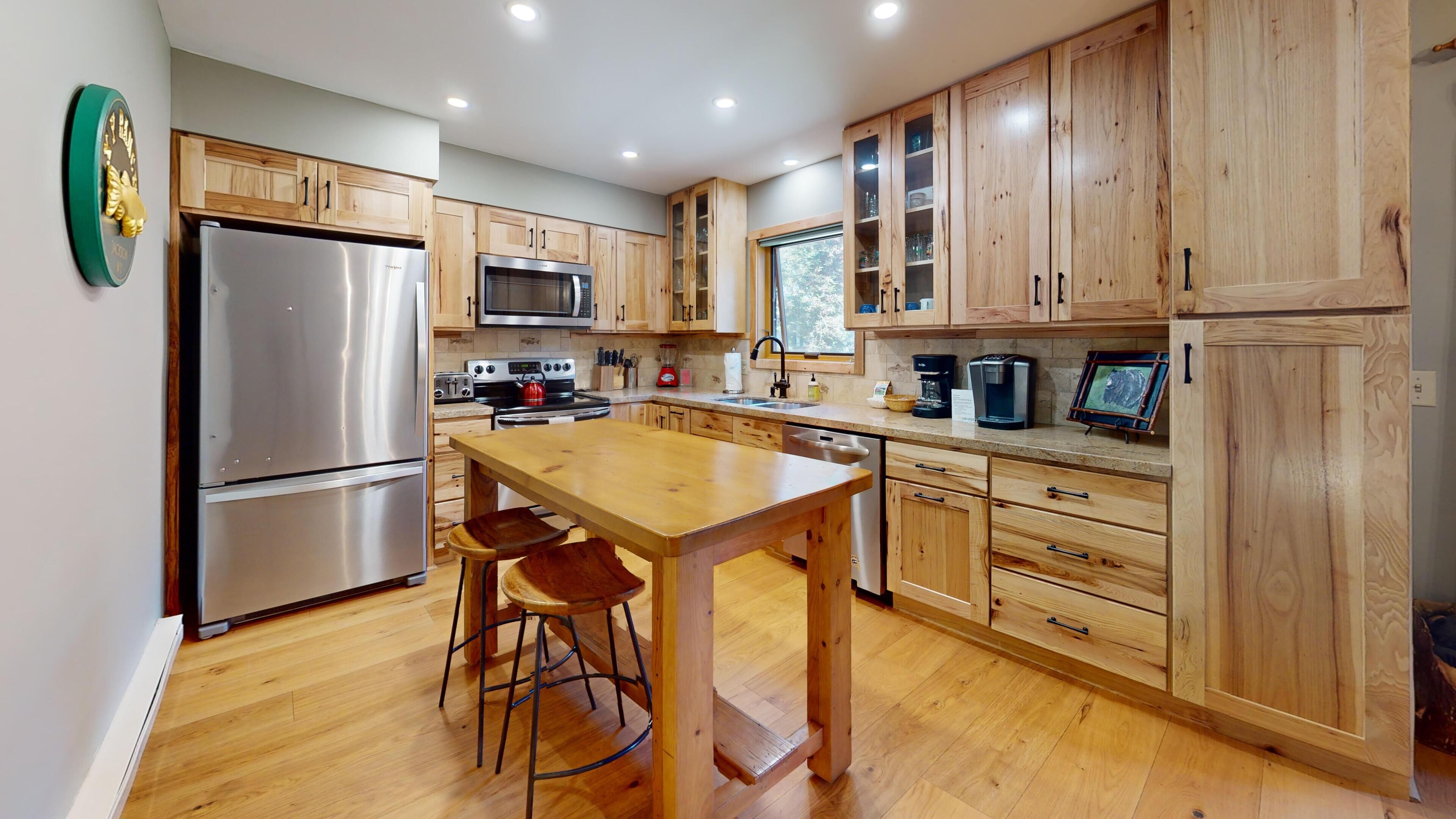 A modern kitchen with wooden cabinets, stainless steel appliances, and a central island with stools.