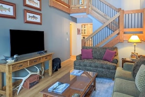Ein Wohnzimmer mit Fernseher, Holzmöbeln, einer Treppe und einer Lampe.