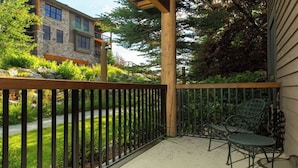 A balcony with a wooden railing, two green metal chairs, and a stone building in the background. - Quaint mountain condo w/two fireplaces, mountain views, balcony & great location (Jackson)