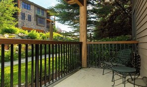 A balcony with a wooden railing, two green metal chairs, and a stone building in the background. - Quaint mountain condo w/two fireplaces, mountain views, balcony & great location (Jackson)