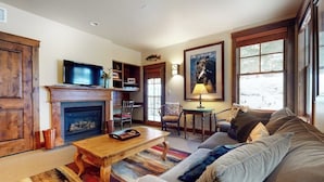 A living room with a fireplace, television, sofa, and a painting on the wall. - Quaint mountain condo w/two fireplaces, mountain views, balcony & great location (Jackson)