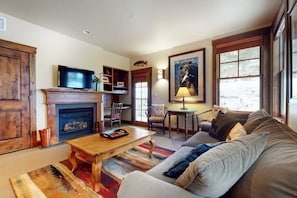 A living room with a fireplace, television, sofa, and a painting on the wall. - Quaint mountain condo w/two fireplaces, mountain views, balcony & great location (Jackson)