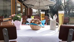 Un espacio de comedor al aire libre con mesas, sillas, jarras de cerveza y una cesta de pretzels.
