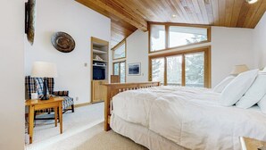 Una camera da letto con un letto grande, un soffitto in legno e una finestra vista alberi.