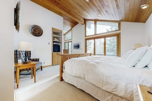 Ein Schlafzimmer mit einem großen Bett, einer Holzbalkendecke und einem Fenster mit Blick auf Bäume.