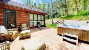 Une cabane en rondins dotée d’un patio aménagé avec des meubles en osier, un jacuzzi et une pièce fermée par des baies vitrées.