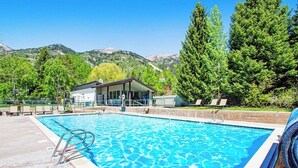 Une piscine avec vue sur les montagnes, un espace couvert avec des chaises et un bâtiment en arrière-plan.