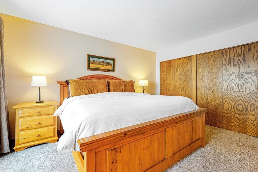 Een houten bed met een witte matras, twee nachtkastjes met lampen, een houten hoofdbord en een wand met een decoratief paneel.