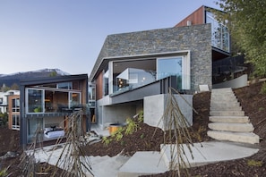 Ein modernes Haus mit Natursteinfassade, großen Fenstern und einer Treppe zu einer Terrasse.