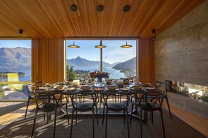 Ein Essbereich mit einem Tisch für sechs Personen, große Fenster mit Blick auf Berge und einen See, Holzboden und moderne Pendelleuchten.