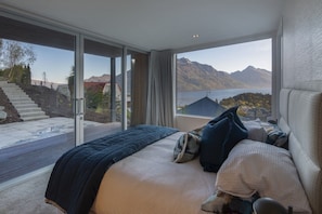 Une chambre avec un grand lit, une vue sur les montagnes et un lac, et un escalier menant à l’extérieur.