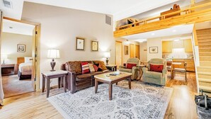 Uma sala de estar ampla com teto alto, um quarto no mezanino, sala de jantar e cozinha.