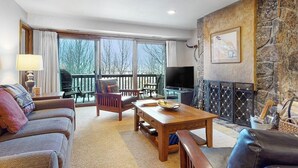 Ein Wohnzimmer mit Kamin, Fernseher und einem Balkon mit Gartenmöbeln.