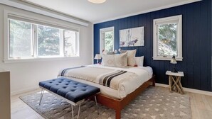 A bedroom with a large bed, a bench, two windows, and a ceiling light.