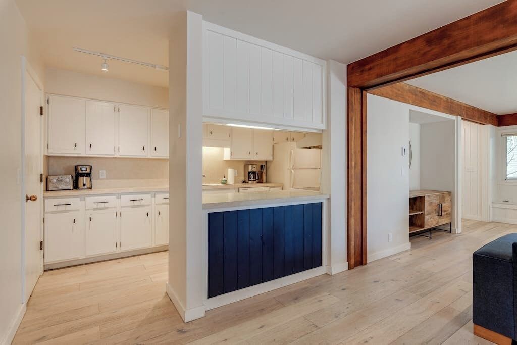 Una cocina moderna con armarios blancos, una pared de acento azul y una viga de techo de madera.