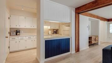 A modern kitchen with white cabinets, a blue accent wall, and a wooden ceiling beam.