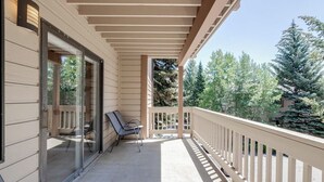 A covered balcony with a railing, a glass door, and two chairs.