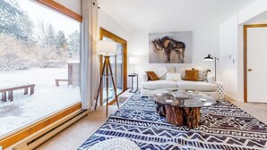 Ein modernes Wohnzimmer mit einem großen Fenster, einem weißen Sofa, einem Couchtisch und einem Gemälde an der Wand.