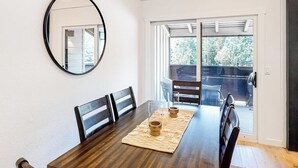 A dining area with a wooden table, chairs, a mirror, and a view through a glass door to an outdoor deck. - Gorgeous, modern mountain view condo with deck & great kitchen (Wilson)
