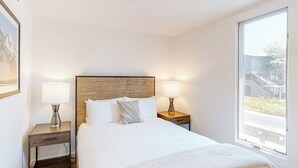 A hotel room with a wooden headboard, two bedside lamps, a large window, and a bed with white bedding. - Gorgeous, modern mountain view condo with deck & great kitchen (Wilson)