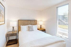 Ein Hotelzimmer mit einem hölzernen Kopfteil, zwei Nachttischlampen, einem großen Fenster und einem Bett mit weißer Bettwäsche.