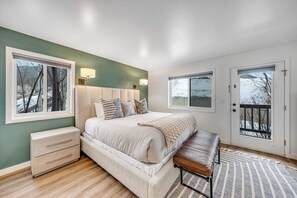 Ein Schlafzimmer mit einem großen Bett, Nachttischen, einer Bank und zwei Fenstern.