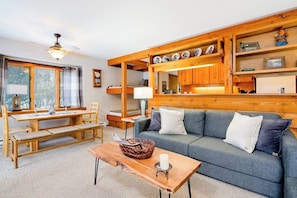 Ein gemütliches Wohnzimmer mit Holzbalkendecke, einer Couch, einem Couchtisch und einem Essbereich mit Tisch und Stühlen.