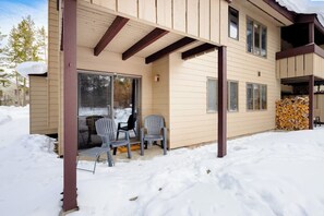 Ein zweistöckiges Haus mit einer überdachten Veranda, einer Schiebetür und einem Holzstoß.