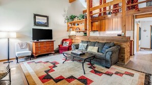 A living room with a sofa, coffee table, TV, and wooden shelves. - Lovely condo with fireplace, skiing, balcony, full kitchen & washer/dryer (Wilson)