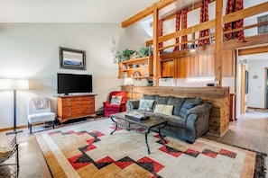 A living room with a sofa, coffee table, TV, and wooden shelves. - Lovely condo with fireplace, skiing, balcony, full kitchen & washer/dryer (Wilson)
