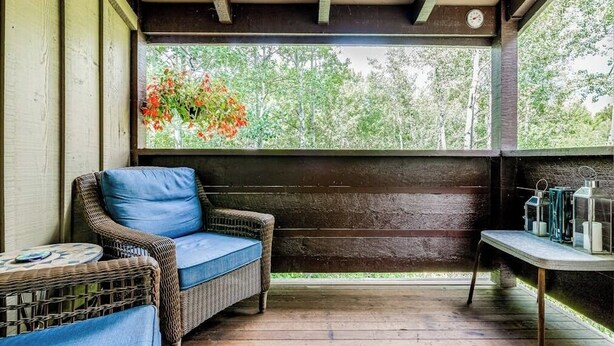 A covered porch with wicker furniture, a table with candles, and a view of trees. - Lovely condo with fireplace, skiing, balcony, full kitchen & washer/dryer (Wilson)